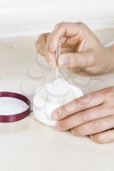 Close up vertical photo of female hands with tweezers pulling out application pad from cosmetic jar

