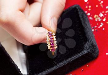 Closeup horizontal photo of female fingers picking up gemstone ring from Jewelry box on red background 
