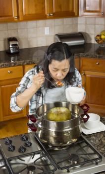 Vertical photo of mature woman tasting winter melon dinner, from steaming pot, with large spoon in one hand and a white bowl in the other hand 