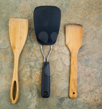 Photo of three kitchen spatulas, two of them wooden, on natural stone