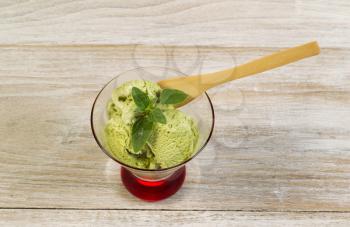 Horizontal photo of green tea ice cream and fresh mint leaf inside of small glass bowl on top of fading white wood boards underneath 