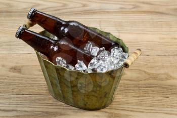 Horizontal photo of glass bottled beer in old metal bucket filled with ice place on rustic wood