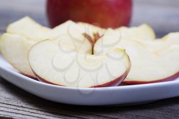 Closeup horizontal photo of fresh apple slices, on white plate, with whole apple and rustic wood in background  