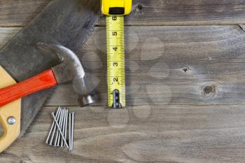 Top view of home repair tools consisting of wood saw, hammer, nails, and tape measure on rustic wooden boards