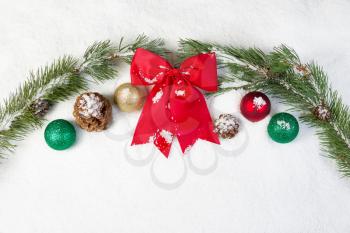 Horizontal view of Red Bow, surrounded by white snow, evergreen tree branches, pine cones and Christmas ornaments 