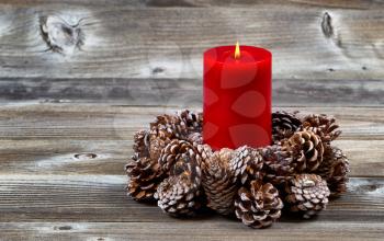 Bright red candle inside of real pine cone wreath for the Christmas season on rustic wooden boards
