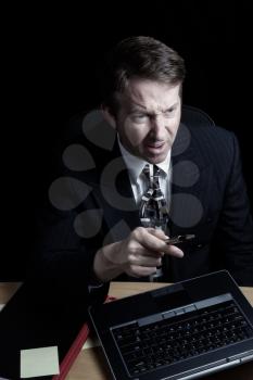 Vertical image of business man, expressing anger while looking at computer screen, working late with black background 