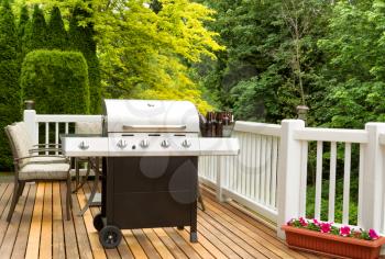 Photo of clean barbecue cooker with cold beer in bucket on cedar deck. Table and colorful trees in background. 