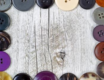 Top view of a clothing buttons in different sizes and colors forming border on rustic white wood. 