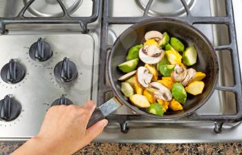High angle view of hand holding frying pan while cooking vegetable in pan on top of stove.