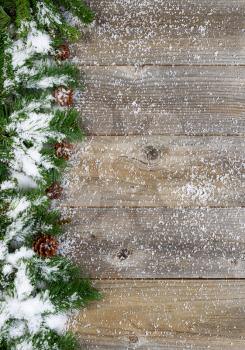 Christmas border with pine tree branches, cones and snow on rustic wooden boards. Layout in vertical format.  