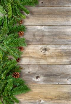 Christmas border with pine tree branches, and cones on rustic wooden boards. Layout in vertical format.  