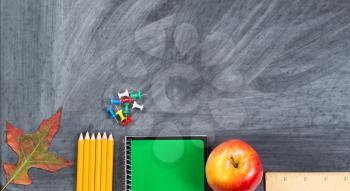 School supplies plus autumn leaf on chalkboard. Back to school concept for fall season with plenty of copy space. 