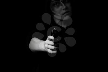 Teenage girl with weapon pointing towards camera in dark background. Selective lighting on hand and weapon. Teen violence concept.