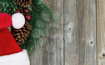 Santa cap and evergreen branch with pine cones on rustic wood. Christmas concept in horizontal layout. 