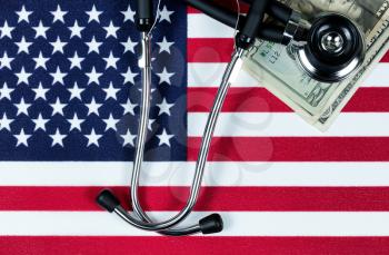 United States of America flag with stethoscope and paper money currency. USA financial health concept. Overhead view in horizontal layout.