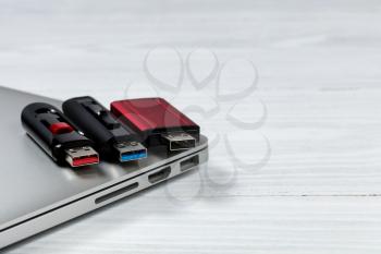 Three thumb drives with different colors inside for USB technologies. Computer and desktop in background. 
