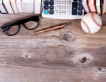 Overhead view of an old paper calculator, books, used baseball, reading glasses and antique pen on rustic wooden boards with available copy space on bottom of part of image.  