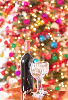 Empty drinking glasses, vintage cork screw and unopen wine bottle on Mahoney table with bright Christmas tree lights in background.  Vertical format layout. 