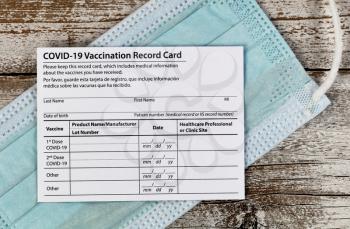 Close up of a Covid 19 vaccination record card place on personal facemask.  Individual record for use during the covid 19 coronavirus global pandemic 