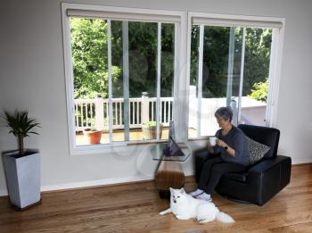Senior woman enjoying her morning coffee while viewing her computer plus having her dog laying near her feet on the hardwood floor