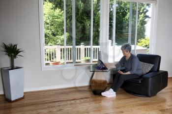 Senior woman looking at her computer screen while at home near the backyard windows   