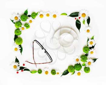 Cup for coffee or tea and glasses with wreath frame from chamomile and chrysanthemum flowers, ficus leaves and ripe rowan on white background. Overhead view. Flat lay.