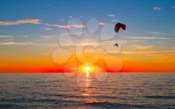 Silhouette of paraglider flying over sea at sunset