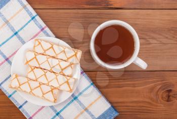 Cup of tea biscuits in a plate and tablecloth on a wooden table.