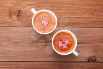 Two cups of tea with lilac flowers on a wooden background.
