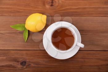 Cup of tea and lemon with leaves on a wooden background. View from above .