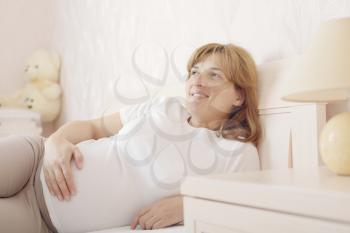 Happy smiling pregnant woman lying on the bed in the bedroom