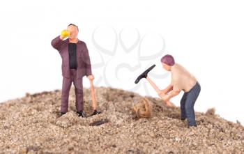 Miniature workers with pickaxes on a mountain of sand