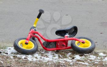 Red childrens balance bicycle at the side of the road
