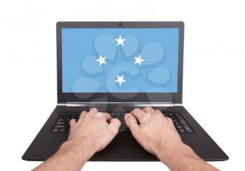 Hands working on laptop showing on the screen the flag of Micronesia
