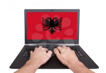 Hands working on laptop showing on the screen the flag of Albania