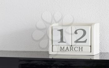 White block calendar present date 12 and month March on white wall background