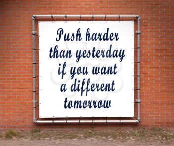 Large banner with inspirational quote on a brick wall - Push harder than yesterday...