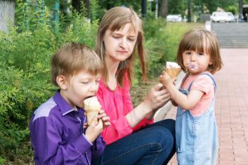 Mother with boy and baby girl sitting in summer park eating icecream