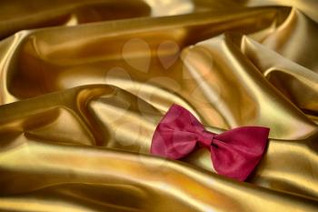 Red bow tie on draped golden satin