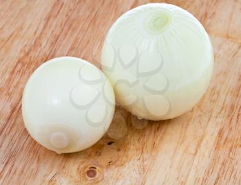 two fresh peeled onions on wooden cutting board