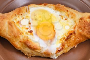 hachapuri by Adzharia (Georgian cheese pastry) , filled with cheese and topped with a soft-boiled egg and butter on ceramic plate close up