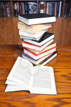 stack of books and open book with blur font on wooden table near bookcases