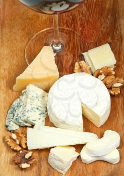 glass of red wine and assorted cheeses on wooden plate close up