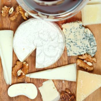 top view of red wine glass and assorted cheeses on wooden plate close up