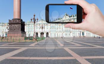 travel concept - tourist shooting photo of Russian state flag on Palace Square, St.Petersburg, Russia on mobile gadget