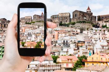 travel concept - tourist taking photo of small sicilian mountain town Castiglione di Sicilia on mobile gadget, Italy