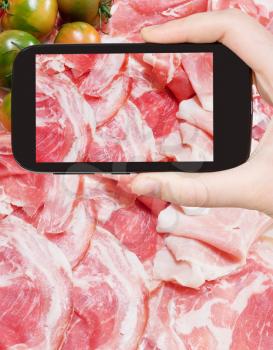 photographing food concept - tourist takes picture of italian prosciutto, pancetta and green tomato on smartphone, Italy