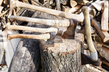 many various axes in wooden block near pile of firewoods