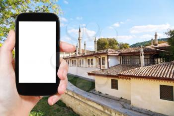 travel concept - tourist photograph moat and walls of Khan's Palace (Hansaray) in Bakhchisaray, Crimea on smartphone with cut out screen with blank place for advertising logo